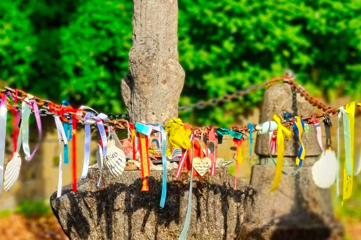 pilgrim shells hanging on a chain fence, around an old stone cross on the trail