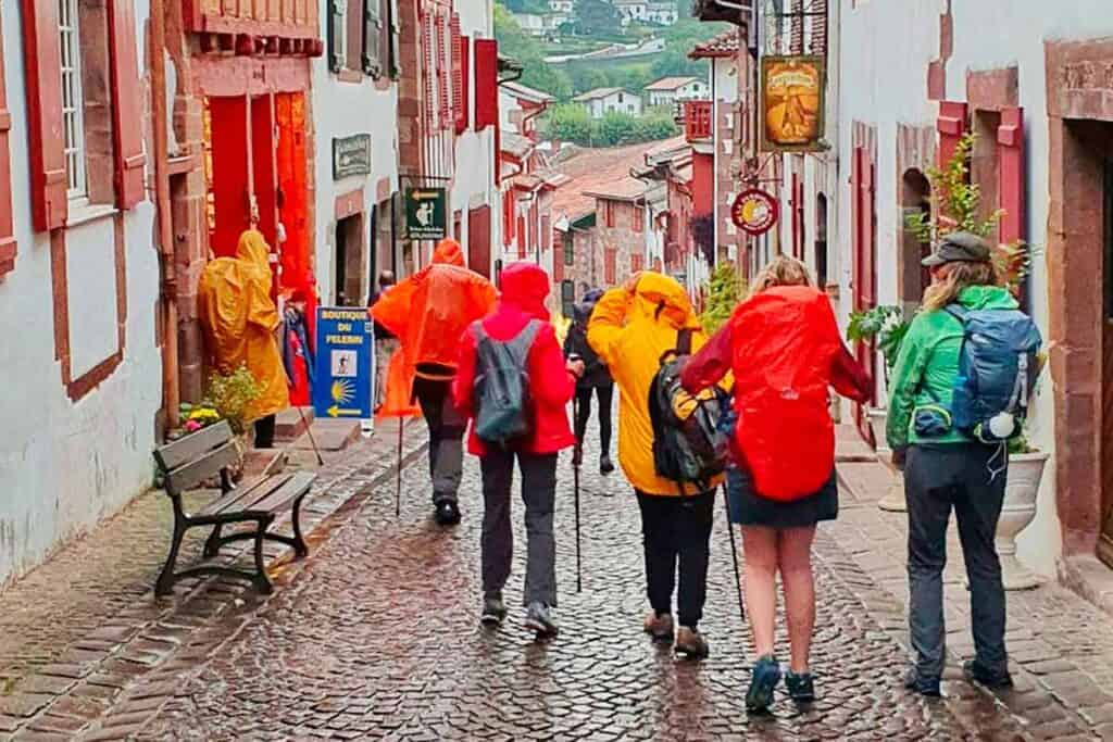 pilgrims in brightly coloured rain jackets and poncho leaving St Jean Pied de Port in the rain