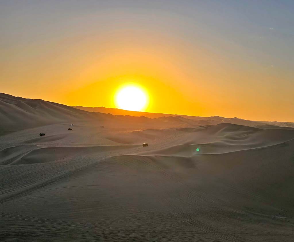 buggies dwarfed by the dunes waiting for the sun to set 
