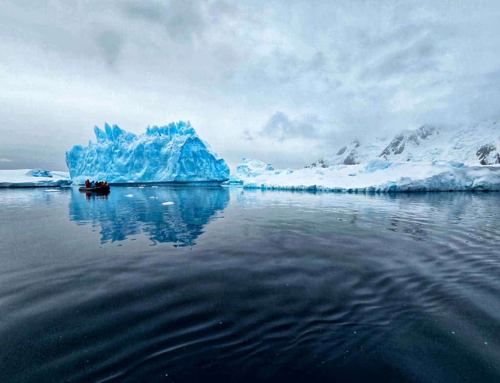 stunning blue iceberg with zodiac dwarfed by it on a calm sea